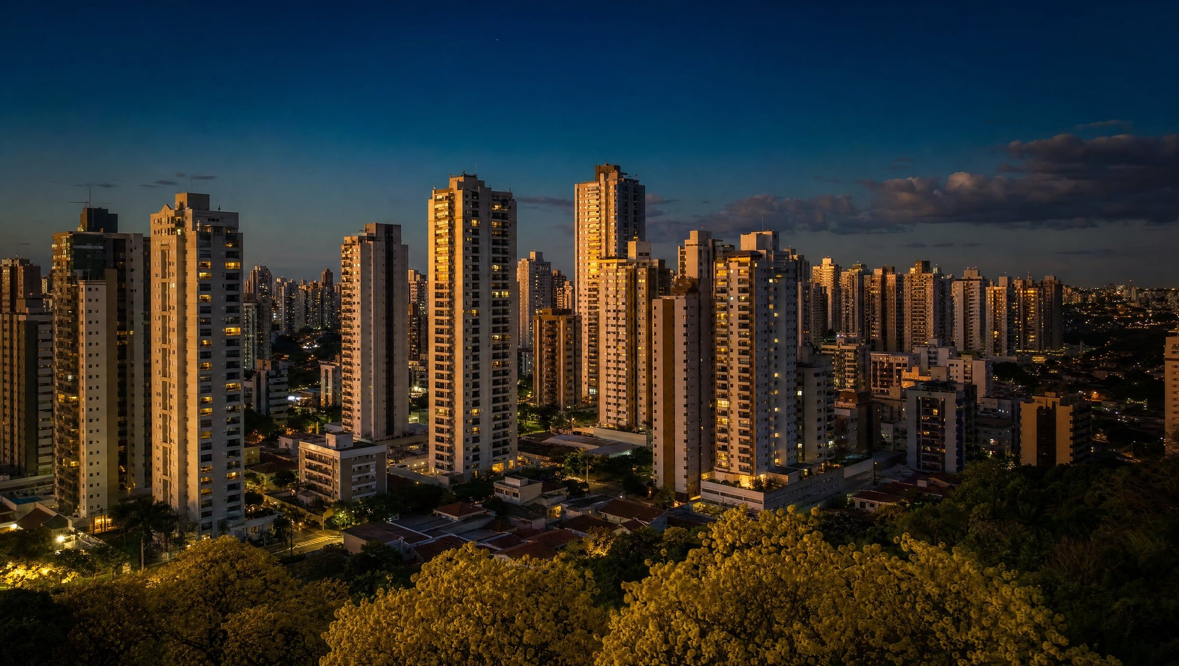 Vista aérea do skyline verticalizado de Ribeirão Preto ao entardecer, com ipês amarelos floridos em primeiro plano